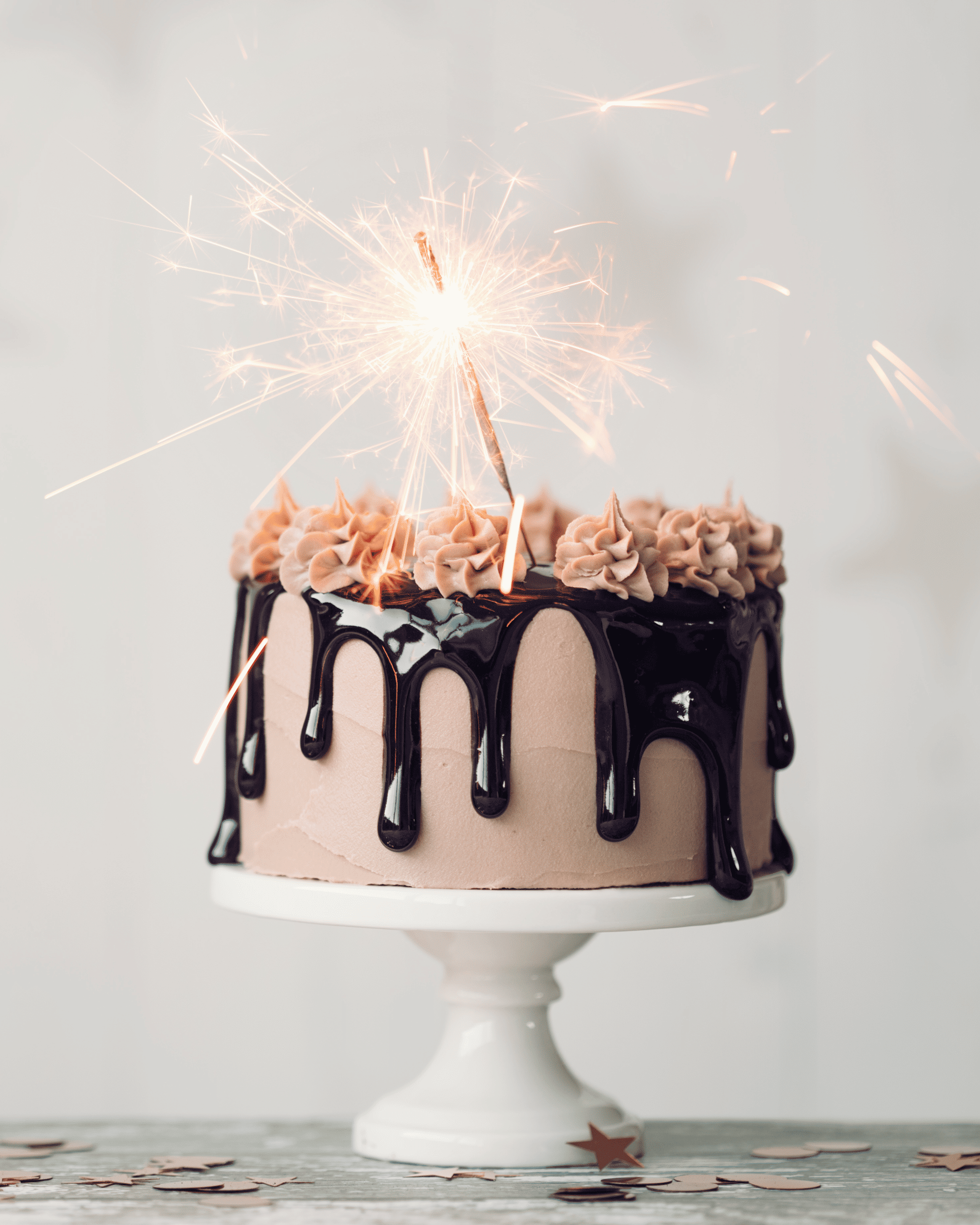 Gâteau et glaçage coulant au chocolat, mousse rose sur le dessus et étincelles.