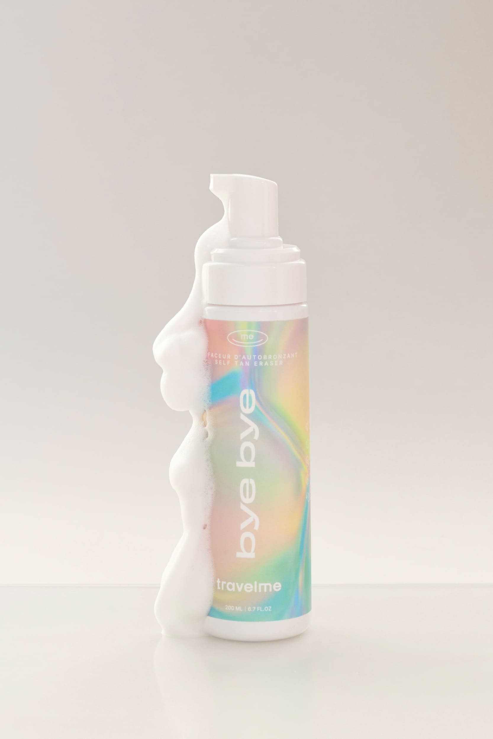 Produit Effaceur d'autobronzant à l'emballage multicolore et métallique, avec de la mousse blanche qui coule, de l'entreprise québécoise TravelMe, sur un fond blanc.