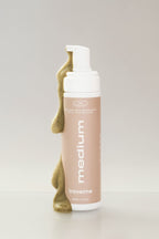 Mousse autobronzante Médium, avec de la mousse qui coule, de l'entreprise québécoise TravelMe, sur un fond blanc.